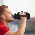 Black AUPET 25oz insulated water bottle sling bag with shoulder strap and two zipper pockets.